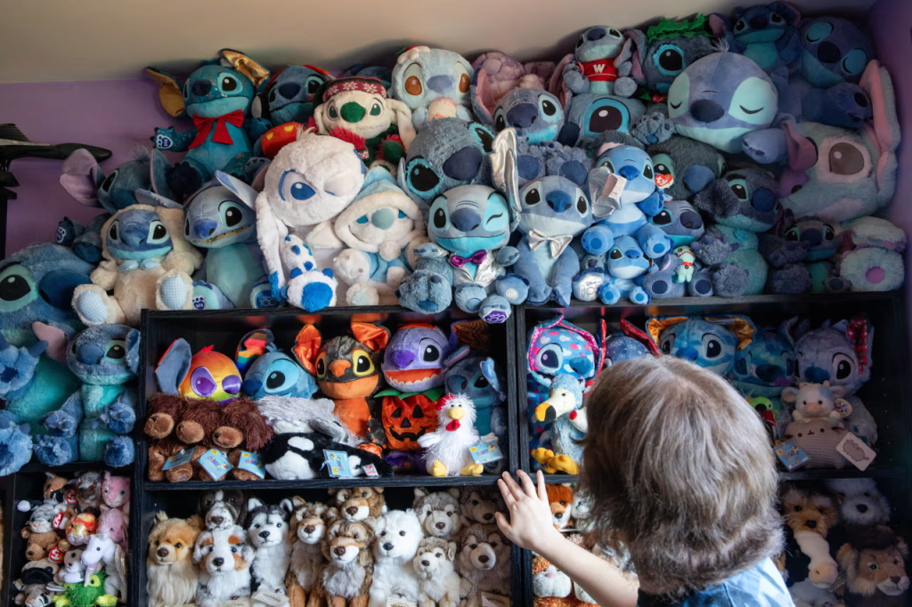 A person looks at shelves filled with a large collection of blue plush toys and other stuffed animals neatly stacked in a room.