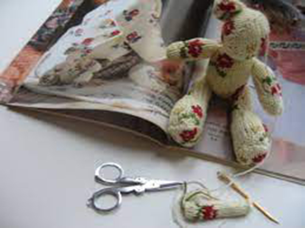 Small floral-patterned teddy bear being hand-sewn beside scissors and needlework materials, showcasing DIY plush toy crafting.