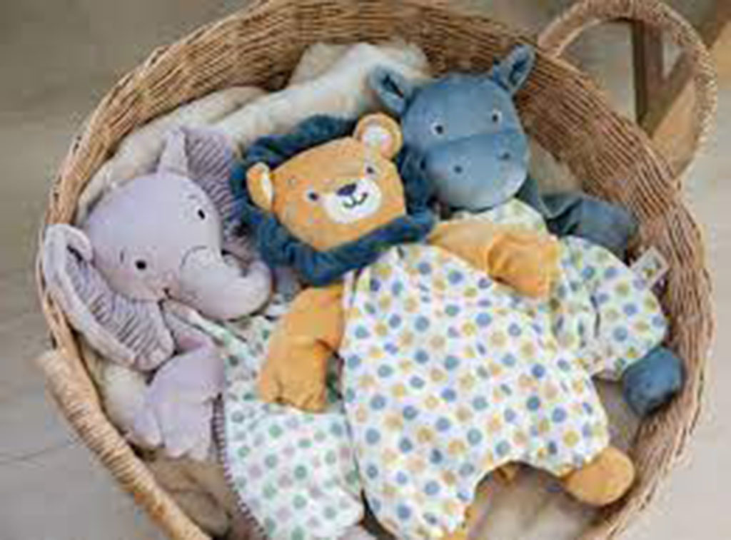 Wicker basket filled with baby plush toys including a lion, elephant, and hippo made from soft, colorful fabrics.