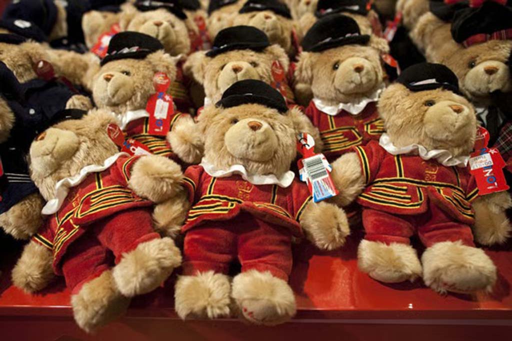 Group of plush teddy bears dressed in traditional red and black Beefeater uniforms neatly arranged for sale on a store display.