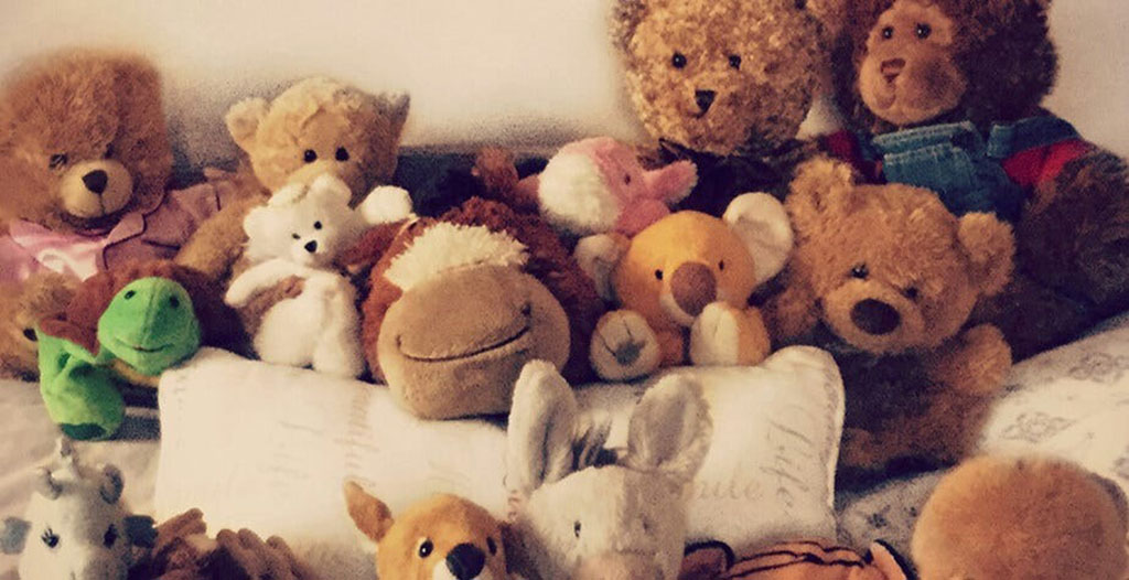 A cozy assortment of plush toys including teddy bears, a koala, a frog, and other stuffed animals arranged together on a bed.