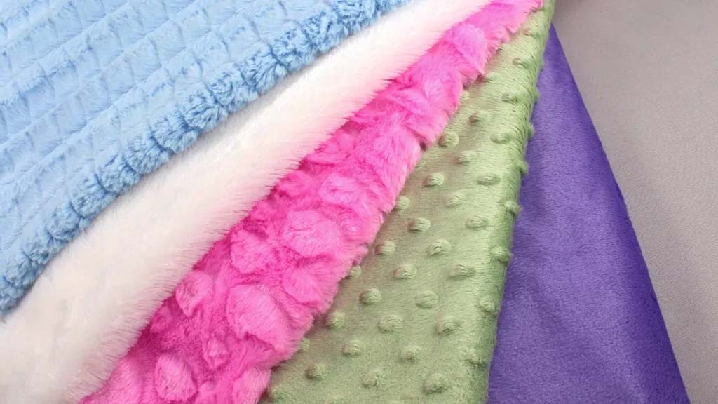 Assorted minky fabrics in blue, white, pink, green, and purple showing various embossed and textured patterns.