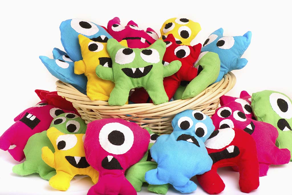 Basket of bright handmade monster plush toys in blue, green, yellow, red, and pink with big eyes and fun expressions.