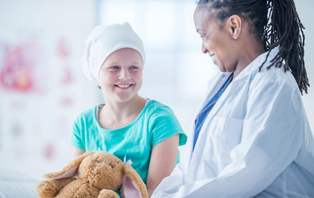 Female doctor smiling at a young patient wearing a headscarf, who is holding a soft brown stuffed bunny, in a bright hospital room.