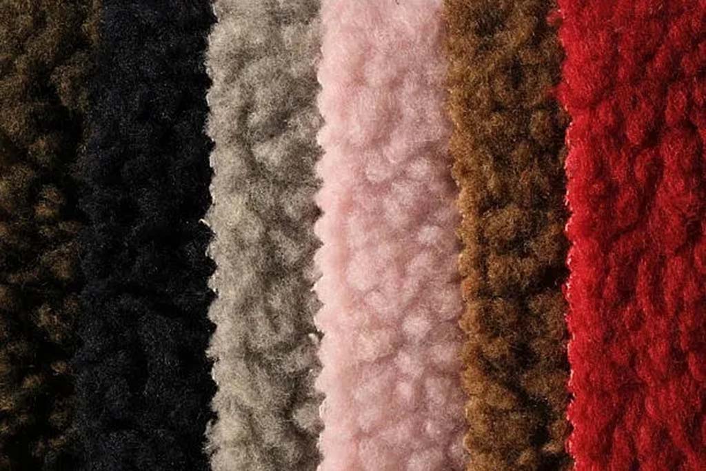 A close-up view of teddy velvet fabric in various colors—black, gray, pink, brown, and red—showing its soft, fluffy texture used in plush toys and upholstery.