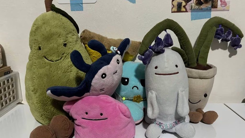 A group of colorful plush toys with playful expressions, including characters shaped like fruits, plants, and animals, arranged on a white table.