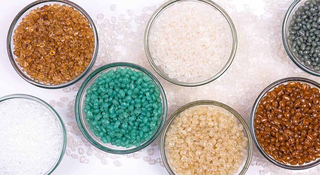 Various colored plastic pellets in glass bowls, showing raw polymer materials commonly used for toy manufacturing and injection molding.