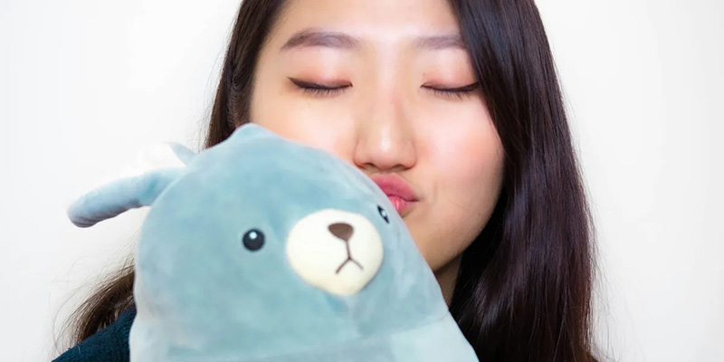 A woman with long dark hair and closed eyes lovingly holding a light blue plush toy close to her face, showing affection and comfort.