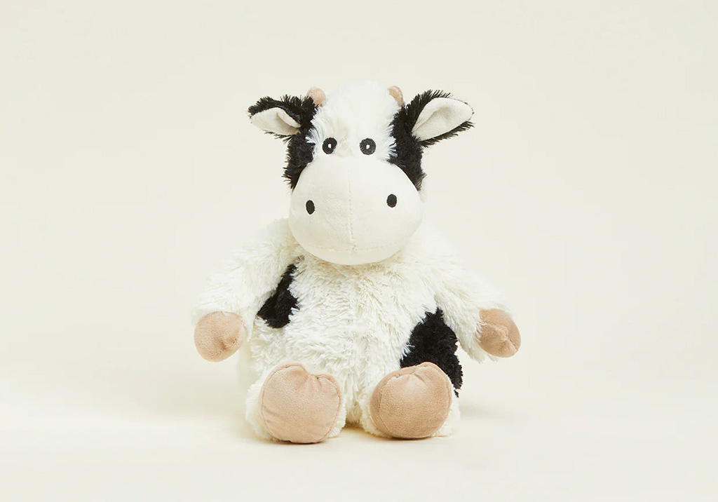 A cute black and white cow plush toy with beige feet and ears sitting upright on a light cream background.