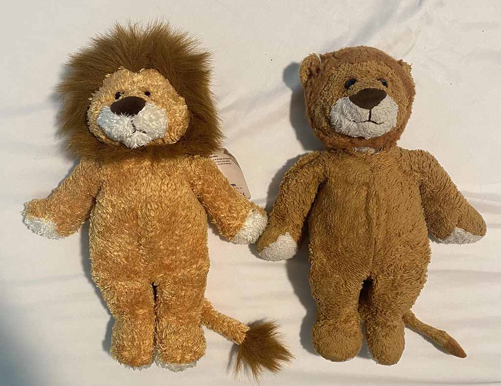 Two lion plush toys side by side on a white surface, one newer with a fuller mane and one older with worn fabric and faded color.