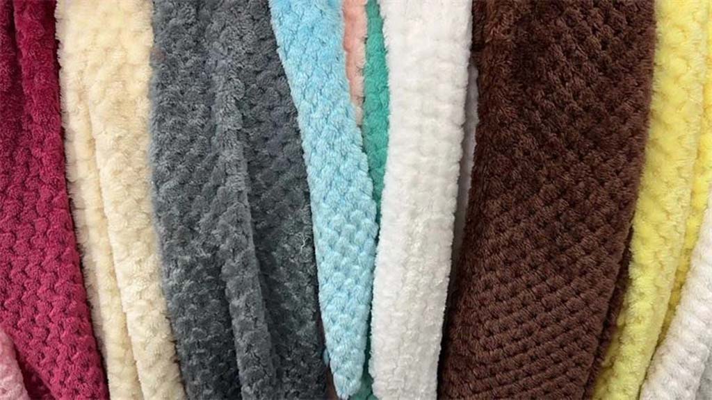 Multiple rolls of textured plush fabric in various colors including red, gray, blue, brown, and yellow, used for teddy bears and stuffed toys.