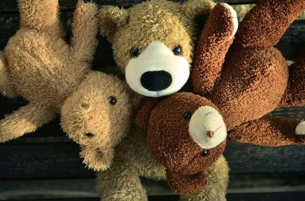 Three soft teddy bears in light brown and dark brown colors lying close together on a wooden surface.