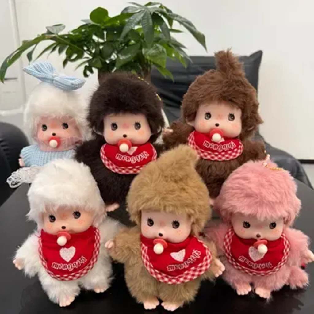 A collection of Monchhichi-style plush dolls with red bibs and pacifiers, dressed in various fur colors, arranged on a table indoors.