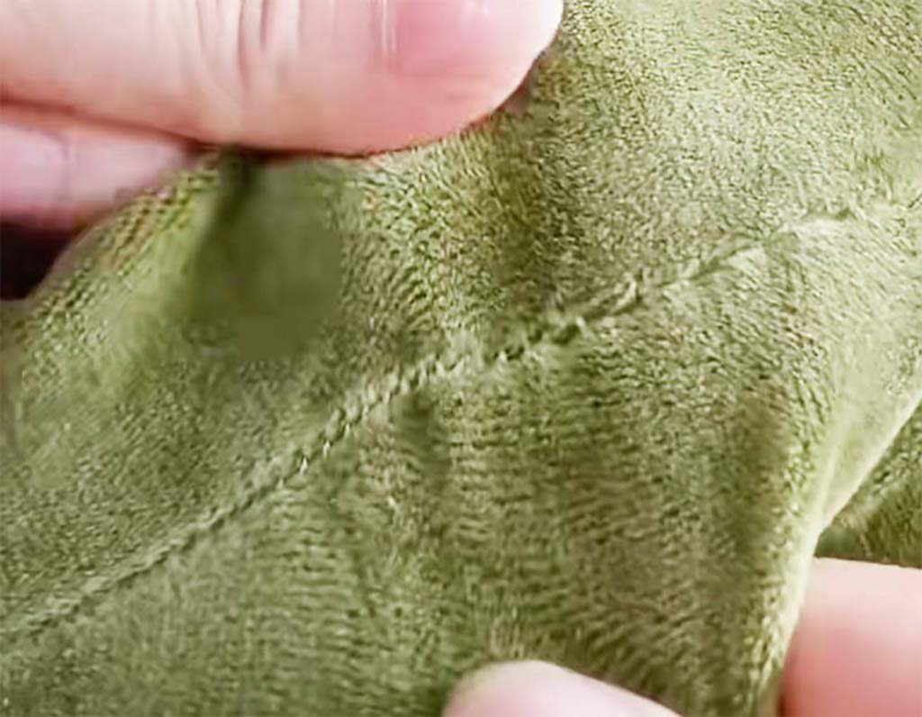 Close-up of hands holding green plush fabric showing a neatly sewn hidden stitch, demonstrating professional sewing technique used in plush toy manufacturing.