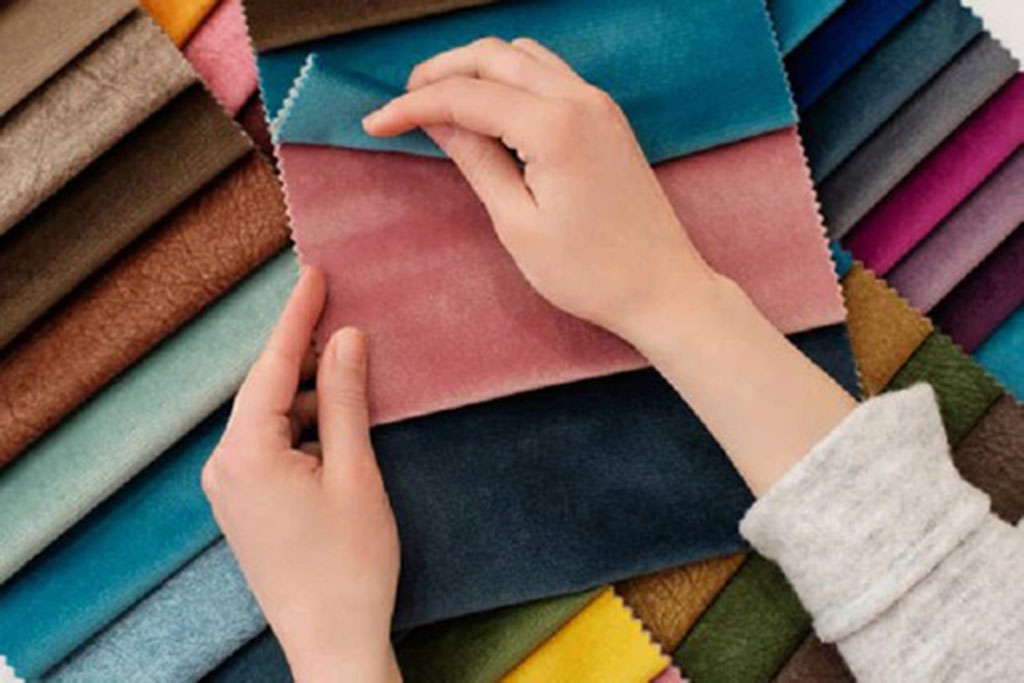 Person examining colorful fabric swatches of different textures and materials for plush toy production quality testing.