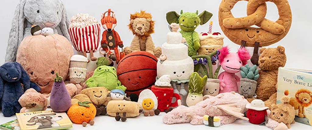 Colorful assortment of plush toys in various shapes like animals, food, and characters arranged together on a white background.
