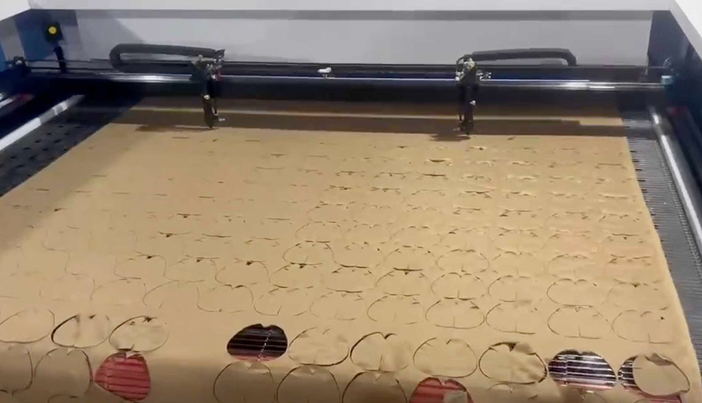 Automated laser cutting machine precisely shaping plush toy fabric patterns on a large sheet for mass production.