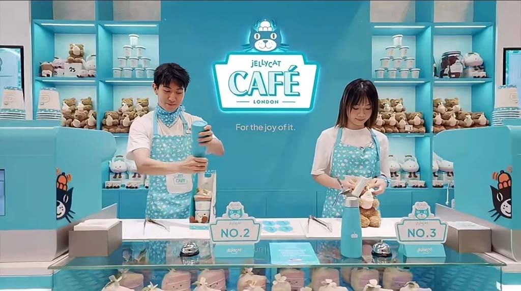 Two staff members preparing drinks and plush toys at the turquoise-themed Jellycat Café counter with branded displays and shelves.