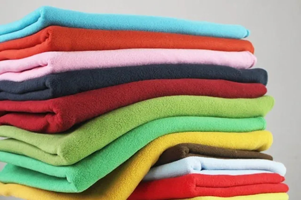 Pile of folded fleece fabrics in assorted bright colors including red, green, yellow, pink, and blue.