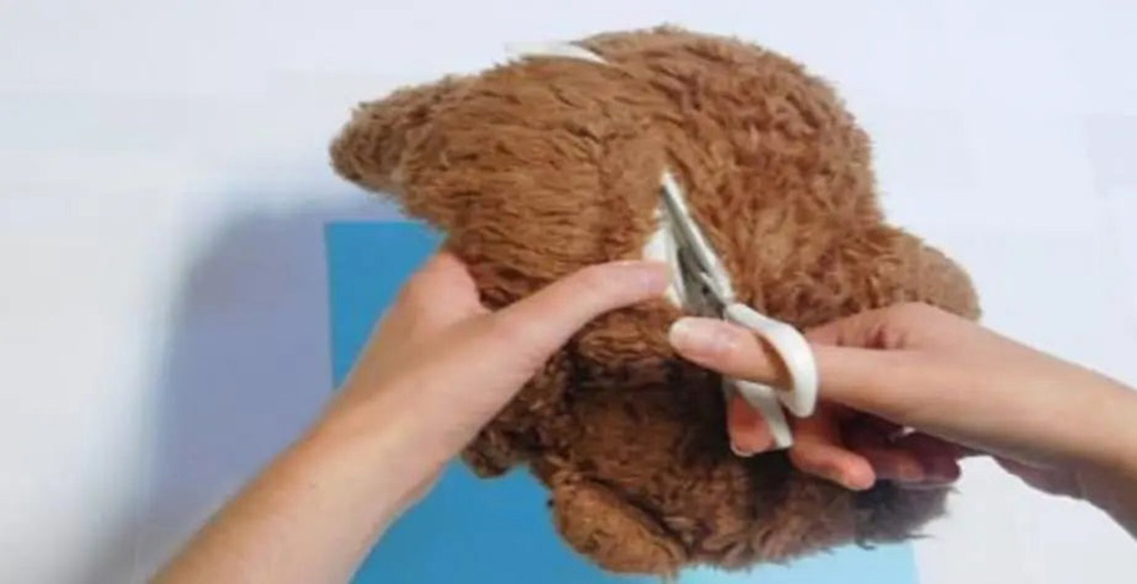 Person using scissors to open a brown stuffed animal for repair or restuffing.