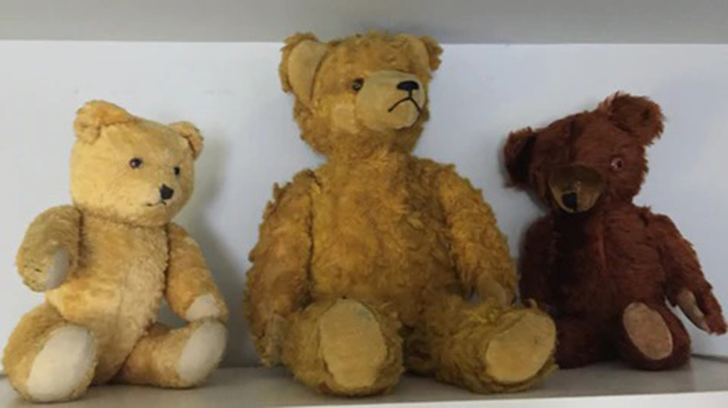 Three old-fashioned teddy bears with worn fur and stitched details sitting on a white shelf, showing classic vintage charm.