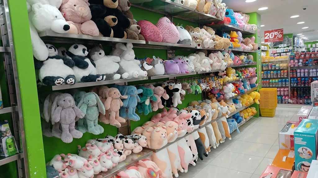 Shelves filled with colorful plush toys including pandas, bunnies, and cows inside a brightly lit toy store.