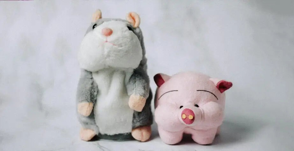 Two cute plush toys, one gray and white hamster and one pink pig, standing together on a light marble background.