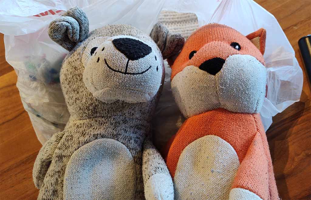 Two knitted plush toys, a gray bear and an orange fox, placed side by side on a wooden surface.