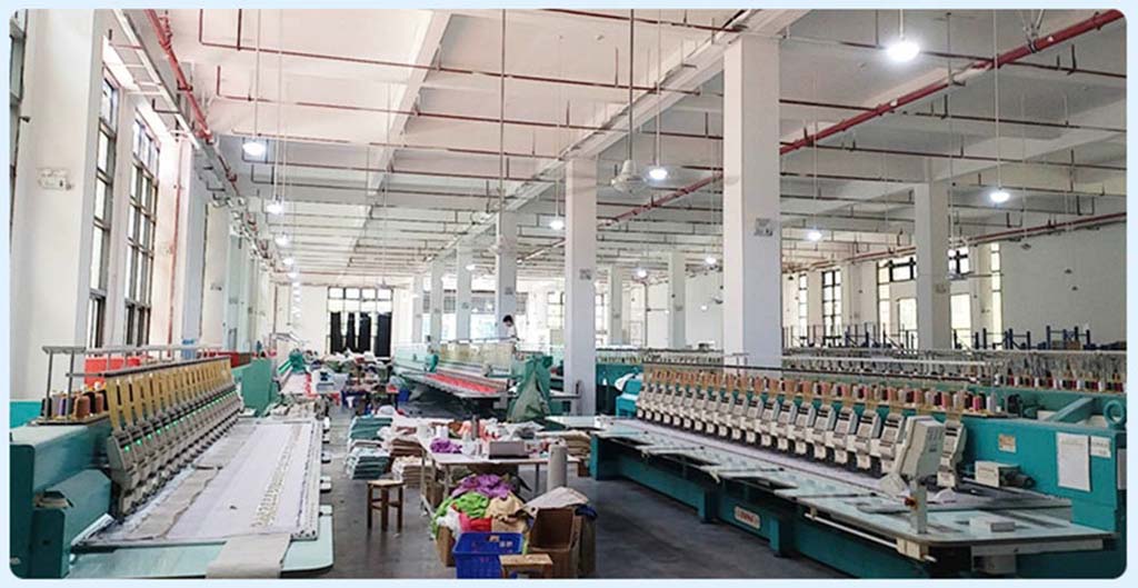 Large embroidery workshop with multiple industrial embroidery machines lined up, used for stitching plush toy fabric pieces in a spacious, well-lit factory.
