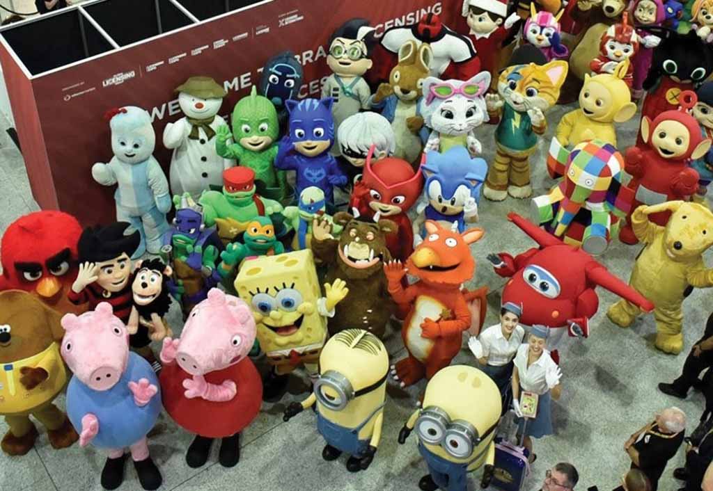 Group of people dressed as famous licensed cartoon and movie characters including Peppa Pig, SpongeBob, Minions, and Sonic at a trade show event.