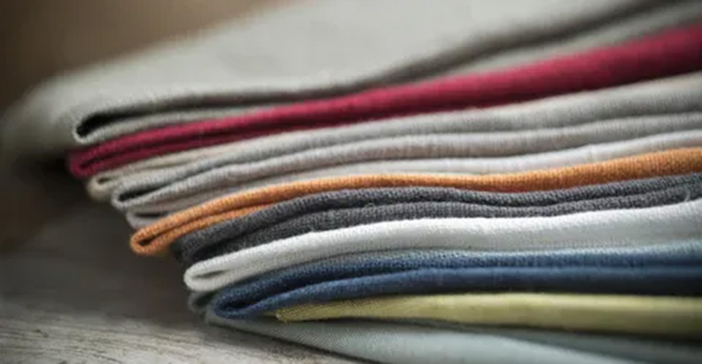 Stack of neatly folded cotton fabrics in assorted colors including red, gray, orange, blue, and white, commonly used in plush toy sewing and textile crafts.