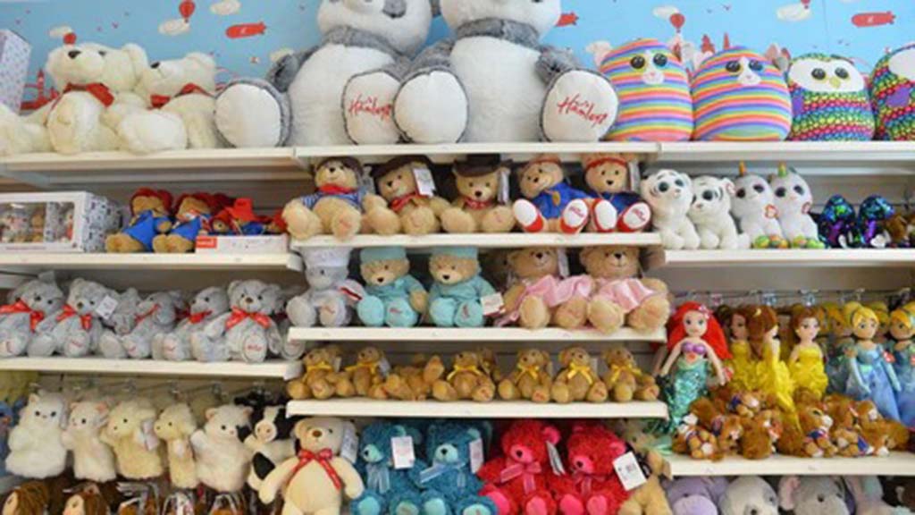 Shelves filled with a variety of plush toys, including teddy bears, dolls, and colorful animal plushies, neatly arranged in a toy shop.