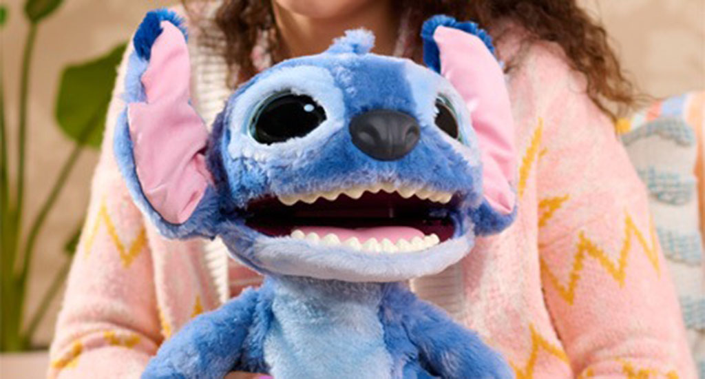 A soft blue plush toy with big black eyes, pink inner ears, and an open mouth showing white teeth, held by a person in a pink sweater.