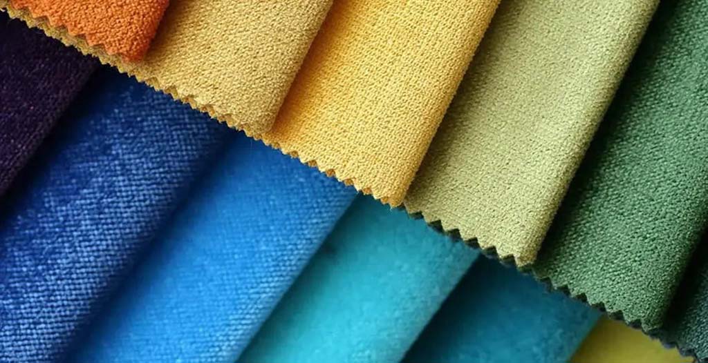 A variety of colorful fabric swatches arranged diagonally, showcasing textures in shades of orange, yellow, green, and blue.