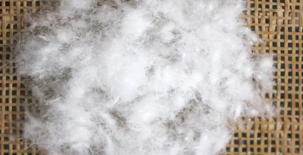 Close-up of white down feather filling material placed on a woven surface used for soft plush toy stuffing.