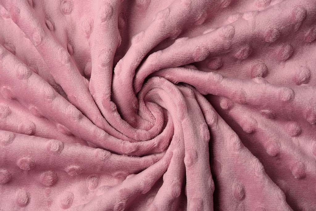 Close-up of pink minky dot plush fabric with soft raised dots and a swirl pattern showing its fluffy texture.