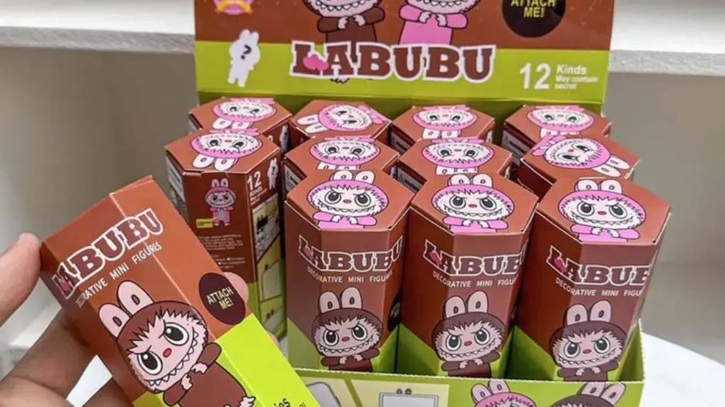 Display of Labubu collectible mini figure boxes with cute bunny-themed character art, showing a hand holding one box from a set of twelve.