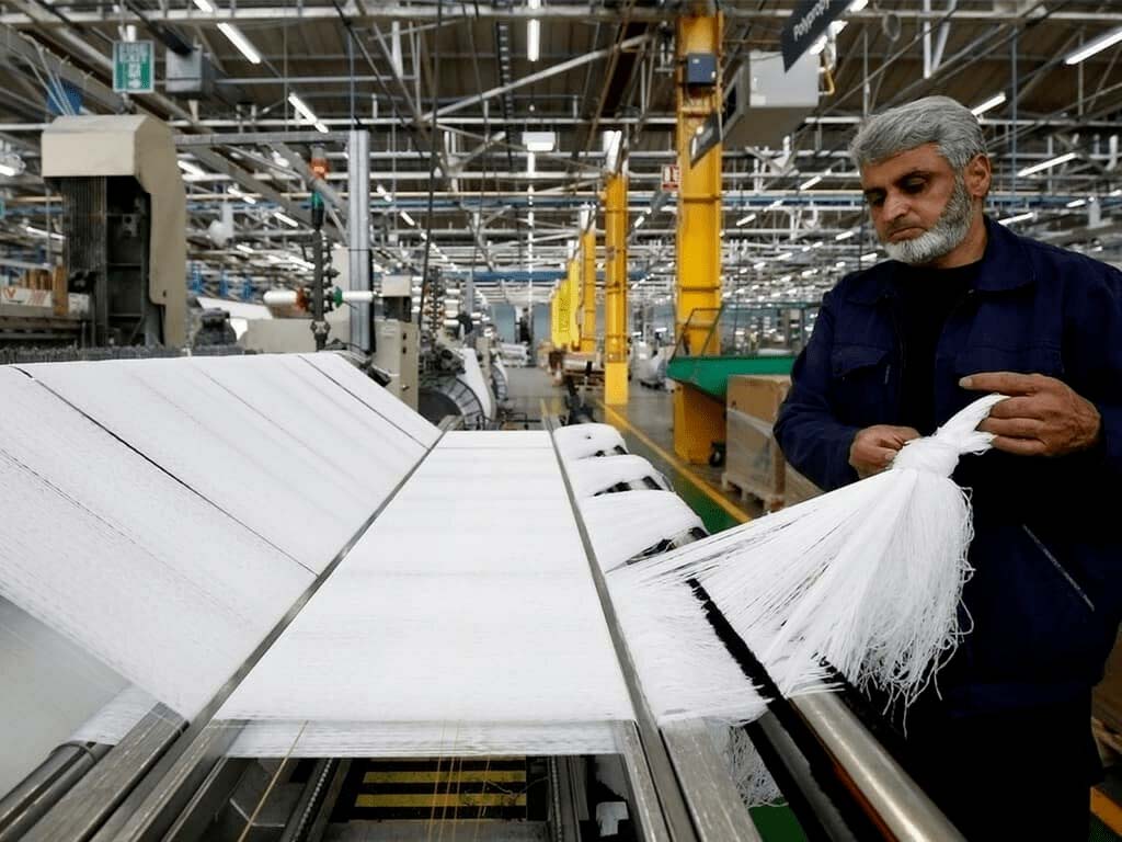 Worker inspecting white synthetic fibers in a modern textile manufacturing factory with automated weaving machines.
