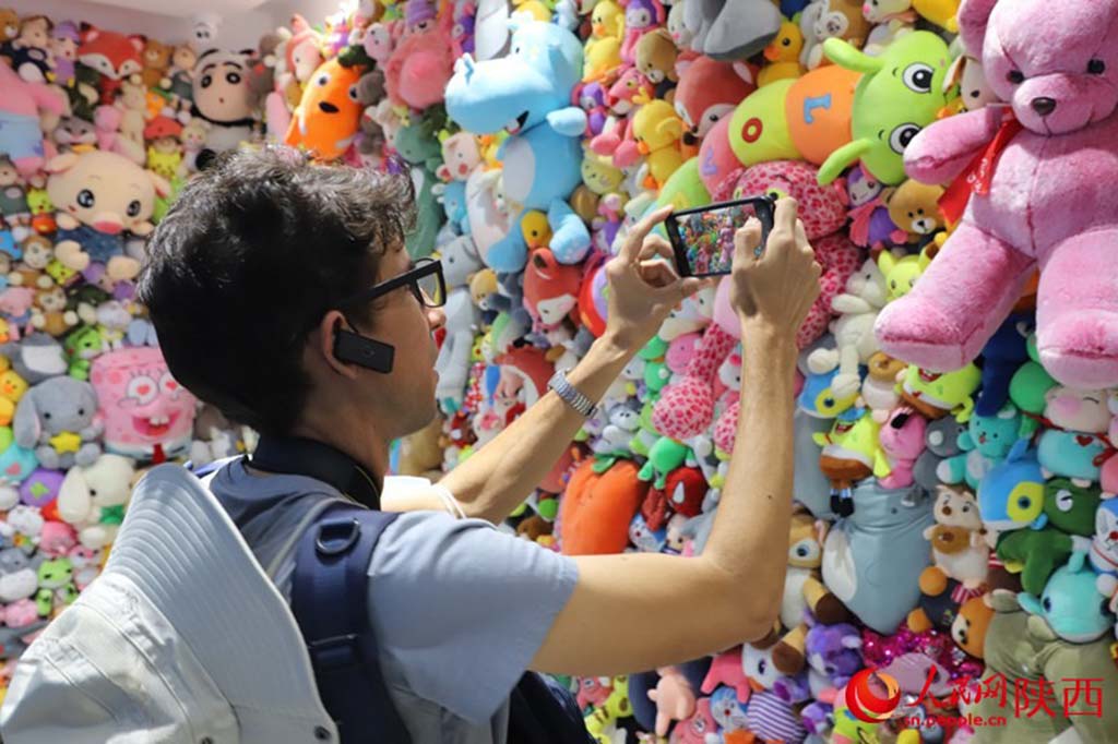 Visitor taking photos of a colorful wall filled with plush toys and stuffed animals at an exhibition or toy market.