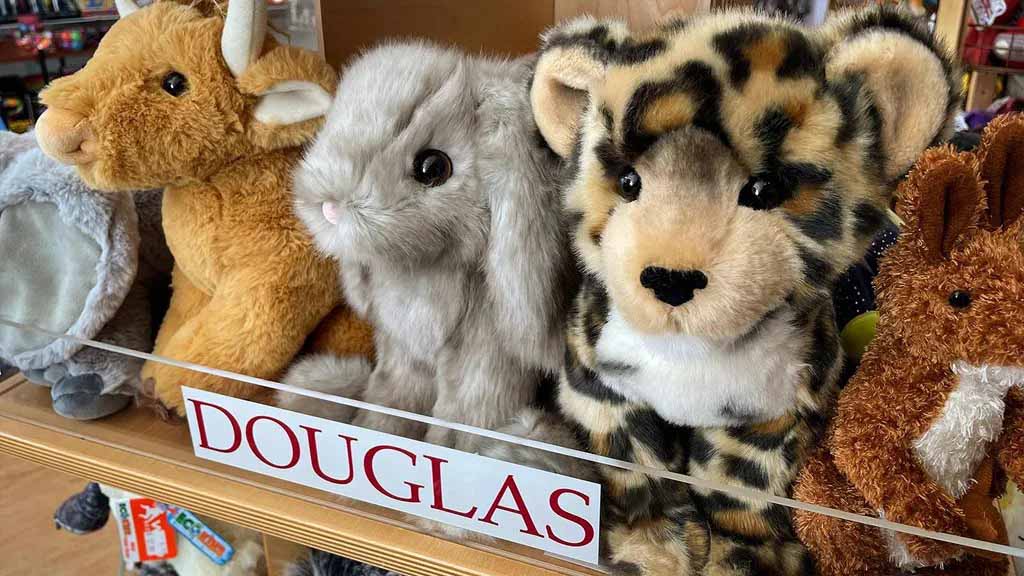 Shelf of Douglas plush animals including a rabbit, leopard, and bull with the Douglas logo visible on the display.