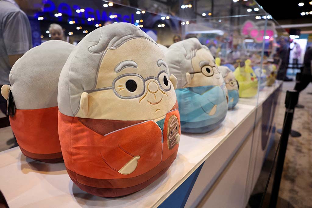 Row of round plush toys with human-like designs and glasses displayed in a glass showcase at a trade show or toy exhibition.