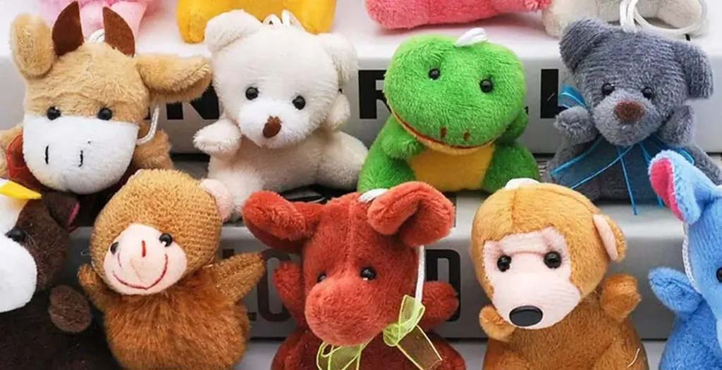 A colorful assortment of small animal plush toys, including bears, monkeys, cows, and dinosaurs, displayed together on stacked boxes.