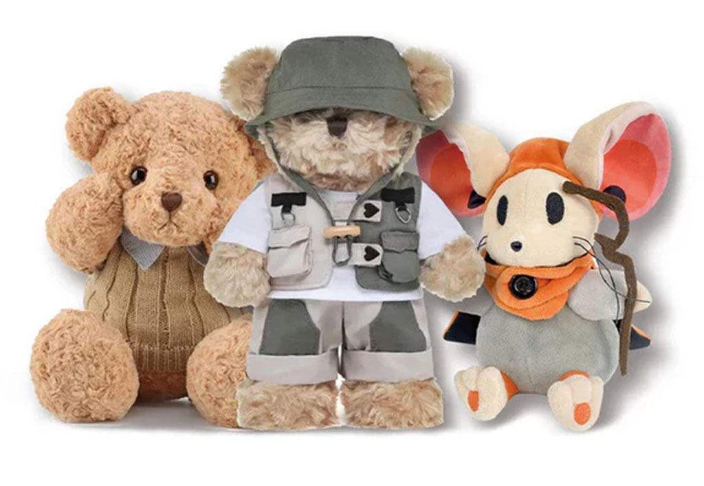 Three plush toys displayed together including a teddy bear in a sweater, a dressed explorer bear, and a mouse character in an orange hood and gray outfit.