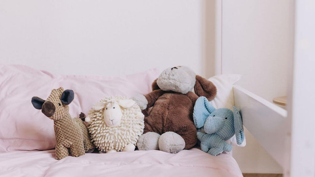 Group of plush toys including a dog, sheep, elephant, and moose sitting on a pink bed.