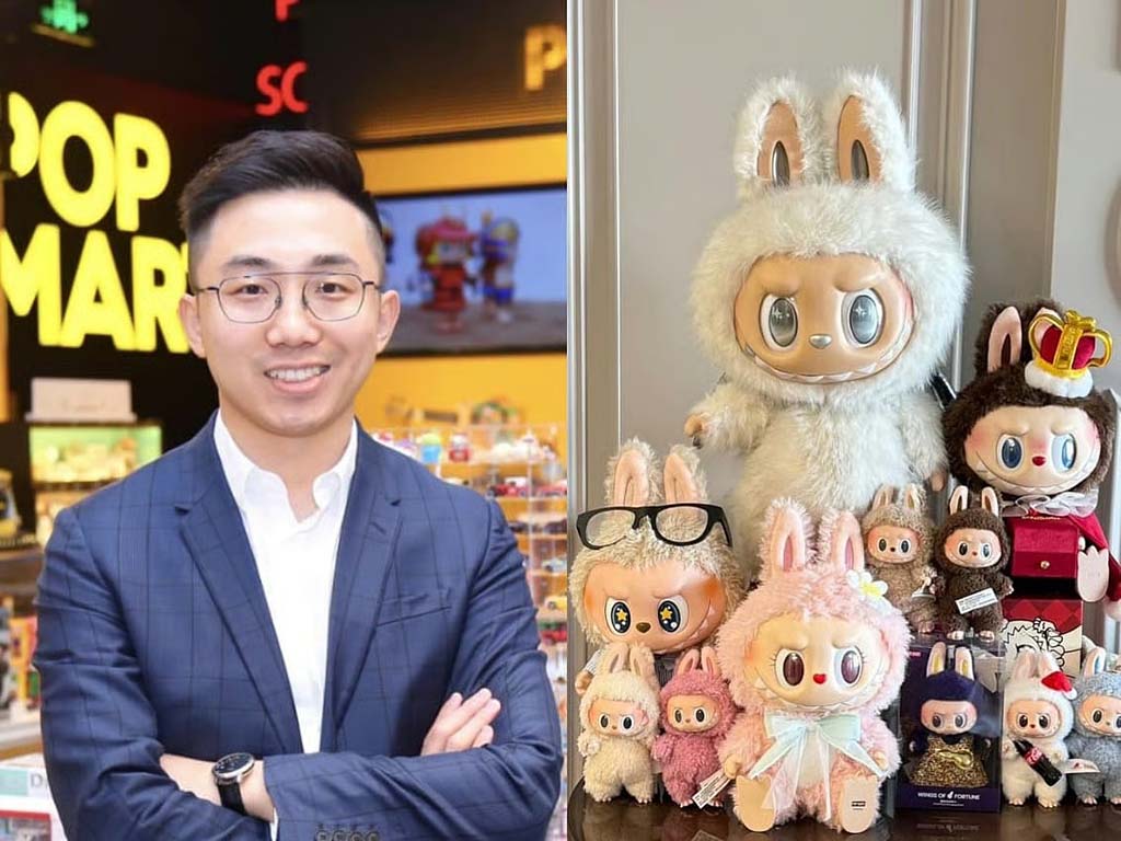 A man in a blue suit standing in a Pop Mart store beside a display of collectible plush dolls, including large bunny-eared figures in various outfits.