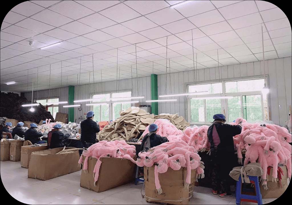 Factory workers assembling pink plush toys in a well-lit production workshop filled with fabric materials and toy parts.