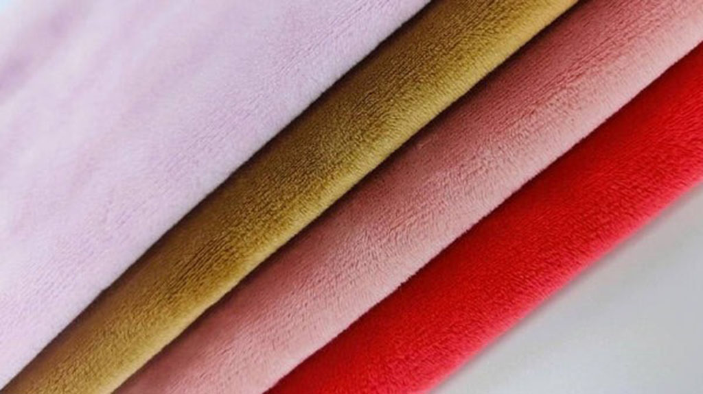 Stack of smooth minky fabric in soft pink, beige, and red tones showing short, velvety texture ideal for plush toys.