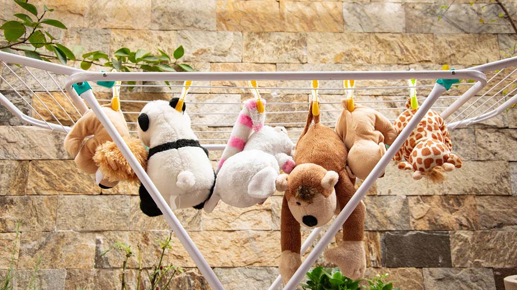 Several plush toys including a bear, panda, and giraffe hanging with clothespins on a drying rack outdoors.