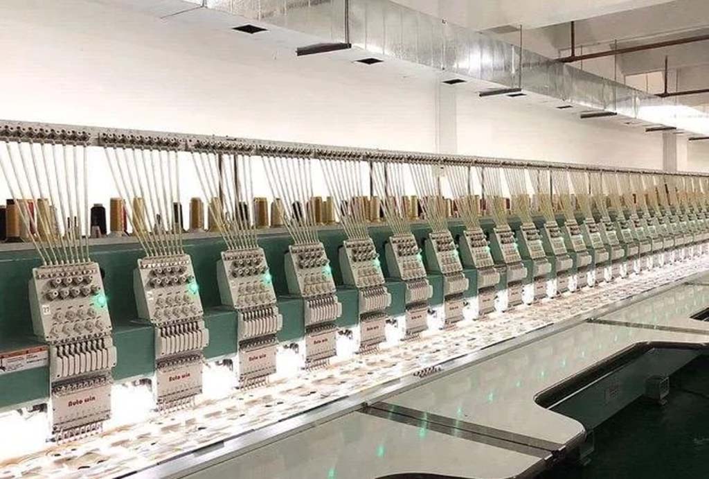 A long row of automated multi-head embroidery machines operating in a plush toy factory for precision stitching and detailing.