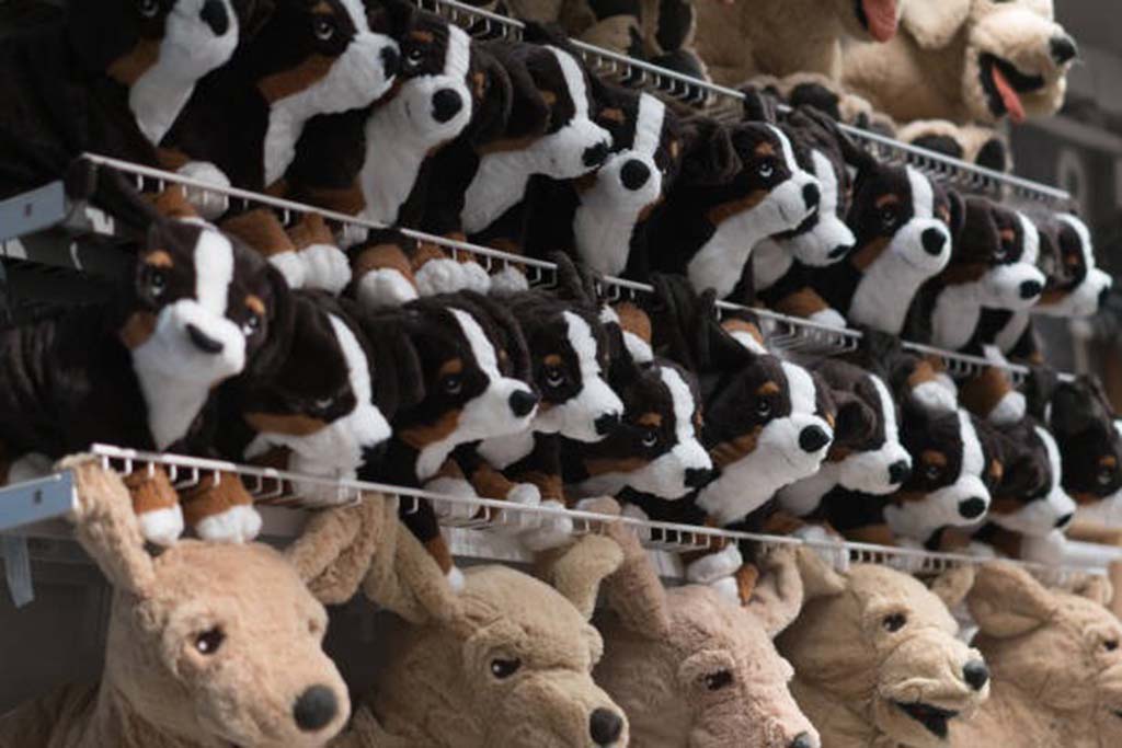 Rows of plush toy dogs and kangaroos neatly arranged on metal display shelves in a store setting.